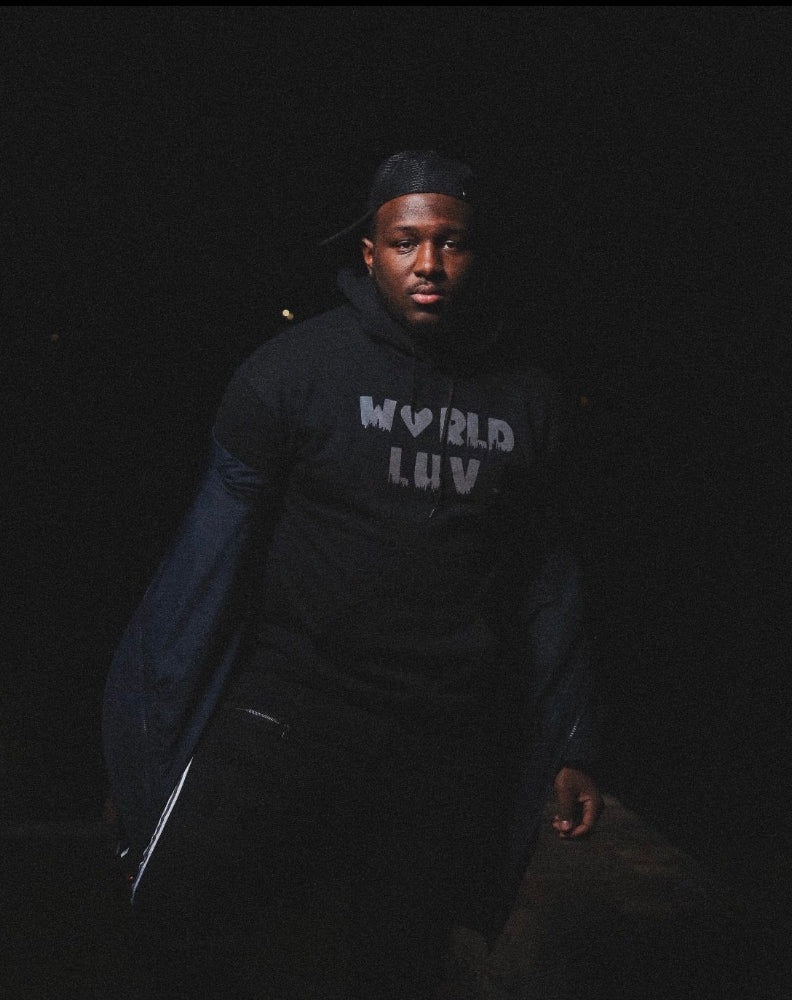 Person wearing a black hoodie with 'World Luv' text in a dark setting