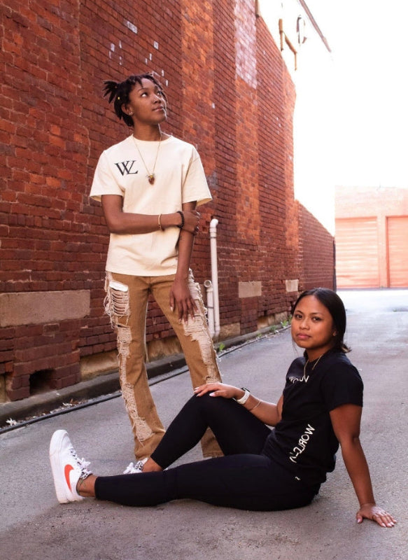 Two women standing against a brick wall in an alleyway.